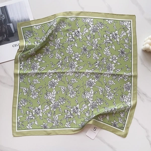 Detailed flat lay of silk-like green square scarf with white floral print on marble