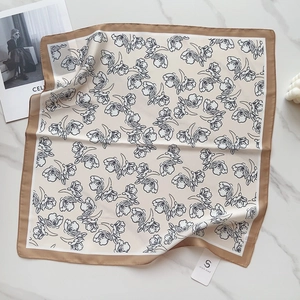 Detailed close-up of a floral silk square scarf with bronze border on marble