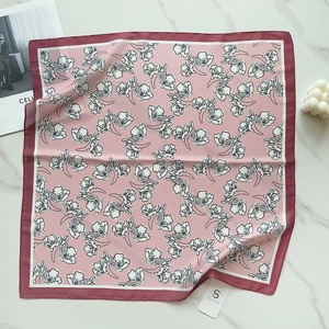 Close-up of pink silk square scarf featuring delicate floral patterns and dark red borders