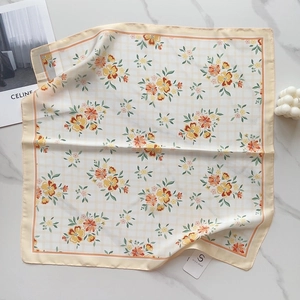 Detailed flat lay of a floral square silk scarf featuring orange blossoms on beige plaid