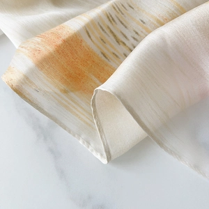 Elegant silk scarf with abstract orange prints and a warm beige base on marble background