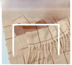 Close-up of the woven texture and fringe detail on a beige and brown plaid scarf