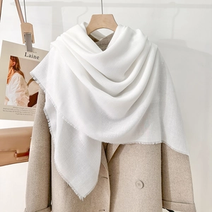 Elegant white square scarf with fringe tassels on a wooden hanger with beige coat
