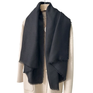 Elegant black solid color shawl scarf with tassels worn over a beige wool coat