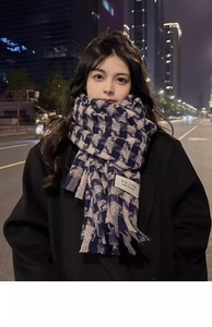 Close-up of thick checkered scarf with tassel edges and branded woven label