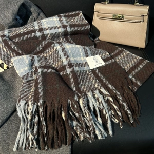Blue and brown plaid winter scarf with fringe tassels on black leather surface