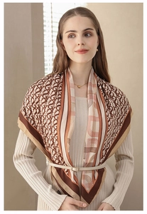 Detail of elegant herringbone letter print silk scarf draped over a beige knit dress
