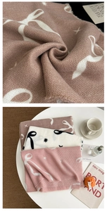 Detail eines weichen Strickschals mit Schleifenmustern und Fransen auf einem warmen Tisch