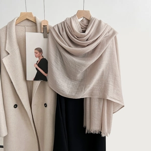 Champagne linen scarf with fringe tassels shown hanging on a beige wool coat