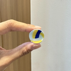 Dettaglio della piccola molletta da pallavolo giallo blu e bianco mostrata in mano