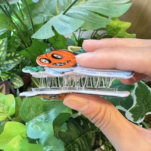 Halloween Haarklammer mit Kürbis- und Geist-Motiv aus Acryl vor grünem Pflanzenhintergrund