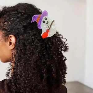 Detail of cute white ghost hair claw with purple witch hat on dark curly hair