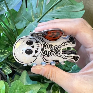 Close-up of a Halloween hair claw featuring a white skeleton holding an orange pumpkin