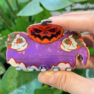 Détail d'une pince à cheveux d'Halloween montrant un fantôme violet brillant et une citrouille