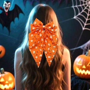 Close-up of bright orange Halloween bow hair clip with ghost patterns on model hair