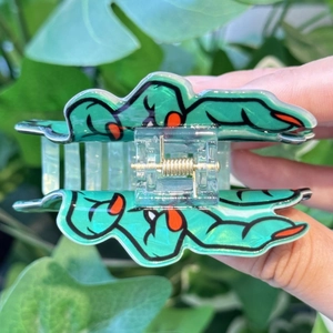 Détail de la pince à cheveux main de zombie verte avec ongles orange dans un jardin