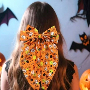 Halloween orange bow hair clip with ghost and pumpkin patterns worn by a model