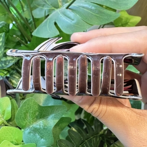 Detail of a dark purple glossy hair claw clip with white trim held against green leaves