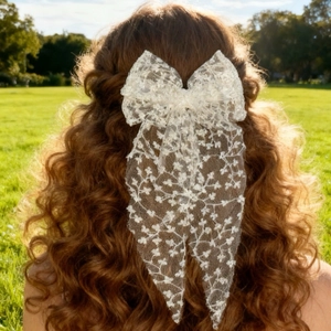 Detail of elegant white lace bow hair clip with long ribbons on model in garden