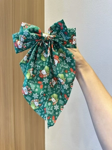 Detail of green Christmas bow hair clip with snowman print and Let it snow lettering