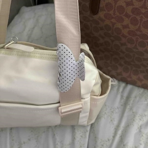 Dettaglio di una pinza per capelli a farfalla bianca a pois neri sulla tracolla della borsa