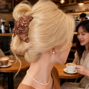 Detail of a brown croissant bow hair claw clip worn on a model in a cozy cafe setting