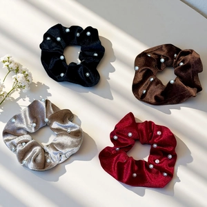 Close-up of velvet pearl scrunchies in black brown silver and red under natural shadows