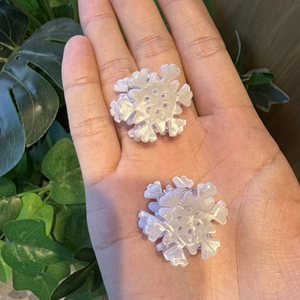 Close-up of dual snowflake-shaped hair clips with white pearlescent resin finish