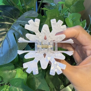 Macro shot of snowflake hair claw clip with white marble texture held in front of greenery