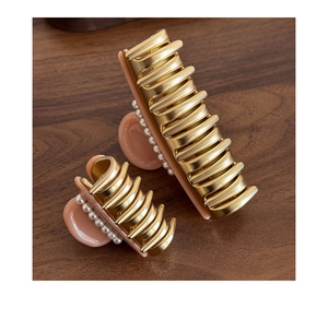Detail of champagne gold acetate hair claws with pearls in two sizes on wood surface