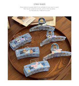 Close-up of five blue denim claw clips with cute cartoon patches on a wooden tray