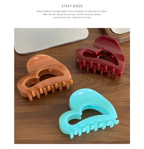 Three heart-shaped claw clips in brown, dark red, and teal on a textured wood surface