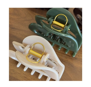 Detail of cream and dark green hair claws with gold springs on a wooden surface