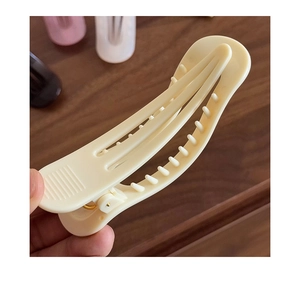 Gros plan d'une grande pince à cheveux jaune crème tenue devant un fond en bois