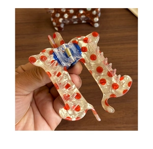 Close-up of a H-shaped hair claw clip with red polka dots on a creamy translucent base