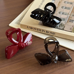 Elegant bow hair claw clips in black, wine red, and amber colors on a wooden surface