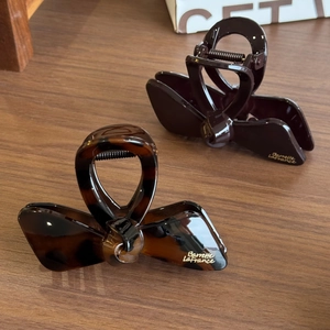 Elegant bow-shaped hair claws in tortoiseshell and dark brown finish on wooden surface