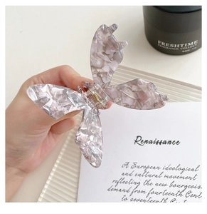 Gros plan sur une pince à cheveux papillon en acétate marbré rose avec un ressort doré