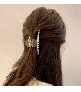 Détail d'une pince à cheveux transparente ornée de perles blanches sur cheveux coiffés