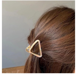 Détail d'une pince à cheveux triangulaire rose effet marbre sur cheveux bruns vue de côté