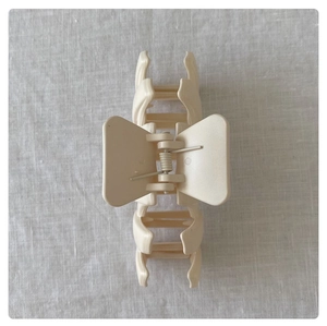 Macro detail of cream matte wavy hair claw clip featuring a silver metal spring mechanism