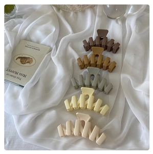 Macro detail of large matte wave hair claws in diverse earth tones on white linen