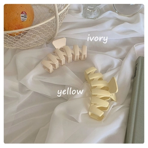 Close-up of matte wave-shaped hair claws in ivory and yellow on white silk fabric