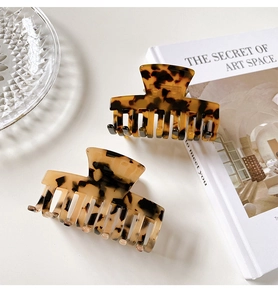 Detail showing two tortoiseshell acetate hair claws on glass plate with aesthetic book