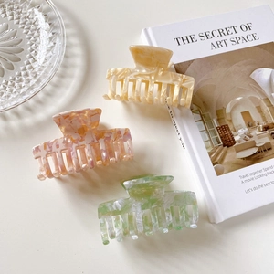 Three large marble pattern acetate hair claws in yellow, orange, and green on a book