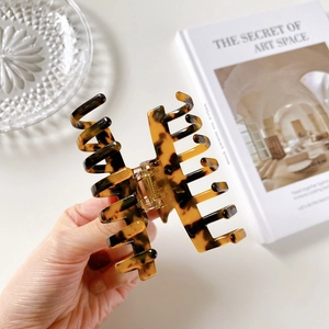 Handheld view of elegant tortoiseshell hair claw clip with a strong golden metal spring