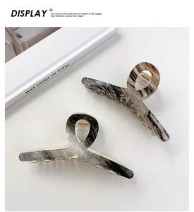 Detail of two marble patterned acrylic hair claws in black and beige on white background