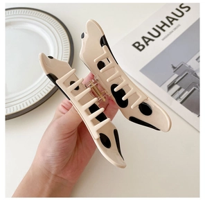 Close-up of beige acetate hair claw clip with black cow print pattern and metal spring