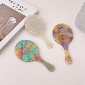 Three acetate oval handheld makeup mirrors with marble texture and wavy edges in bright natural light