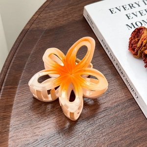 Détail d'une pince à cheveux fleur en résine dégradé orange sur plateau bois